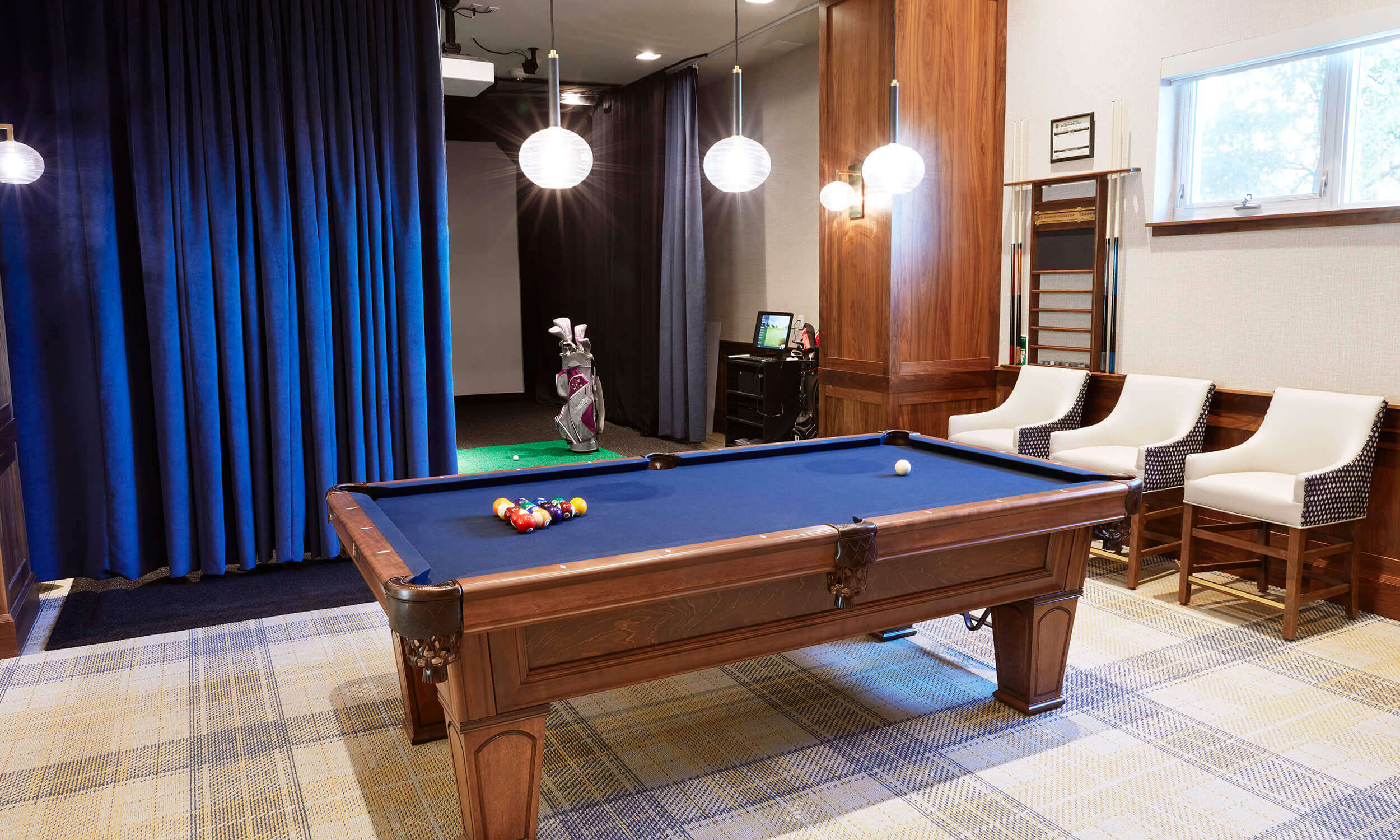 Room with pool table in front of navy curtains and beside three cushioned chairs