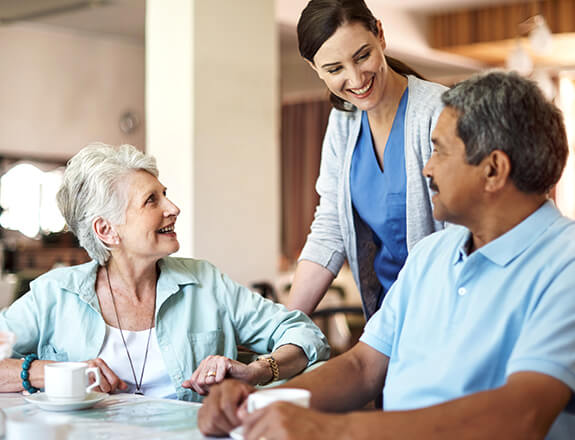Nurse smiling and assisting two residents of retirement home