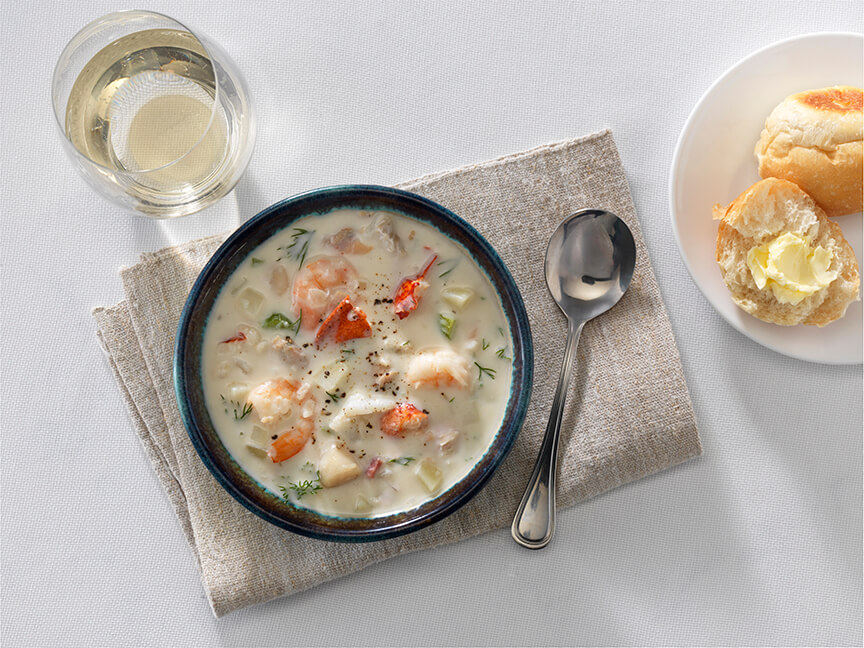 Bowl of chowder soup with glass of wine and dinner roll