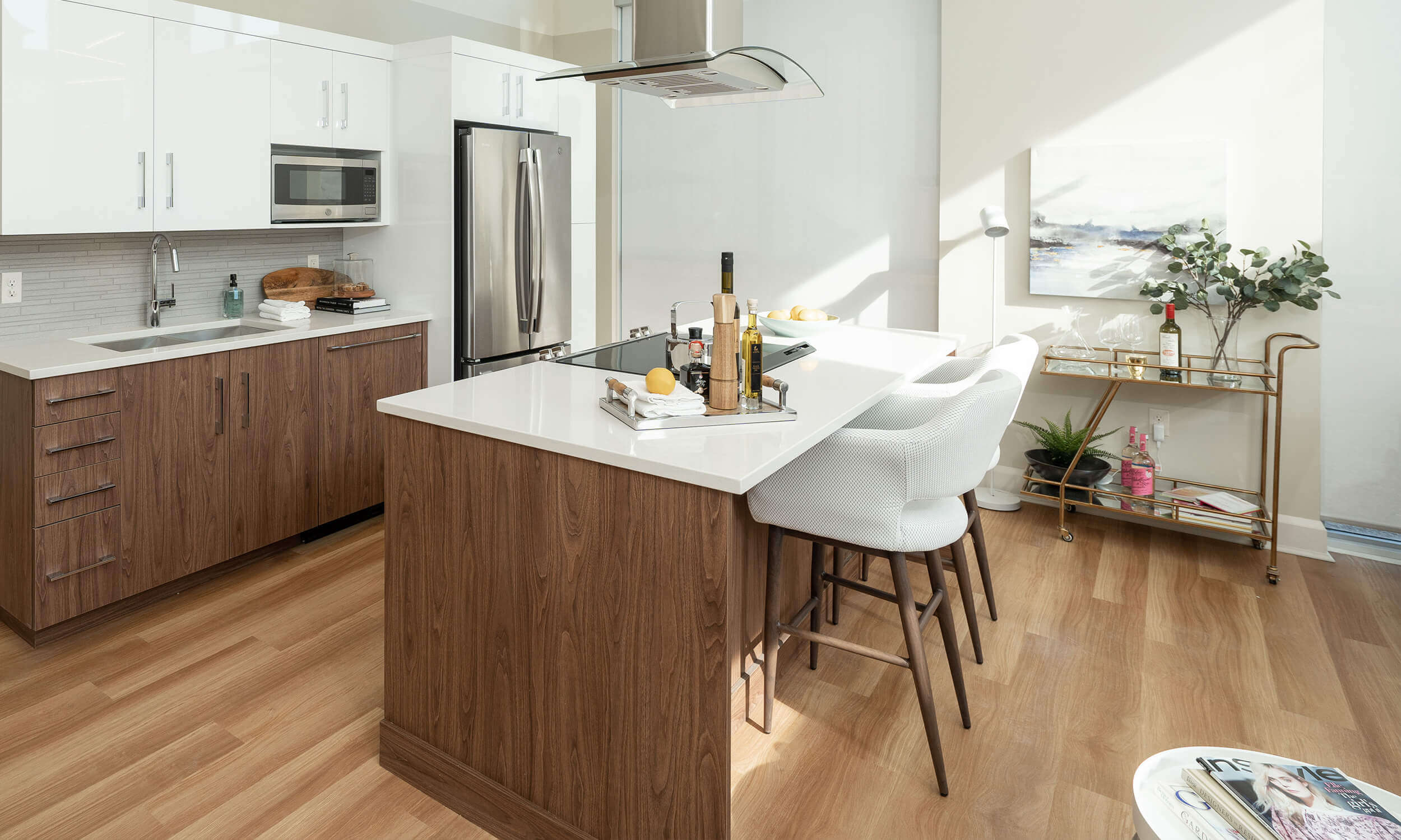 Modern-looking kitchen with white countertops and island with tall chairs and silver appliances