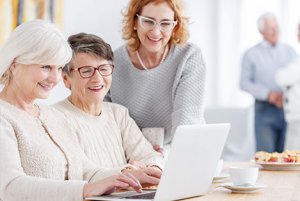 Three senior women looking at laptop together while one woman types