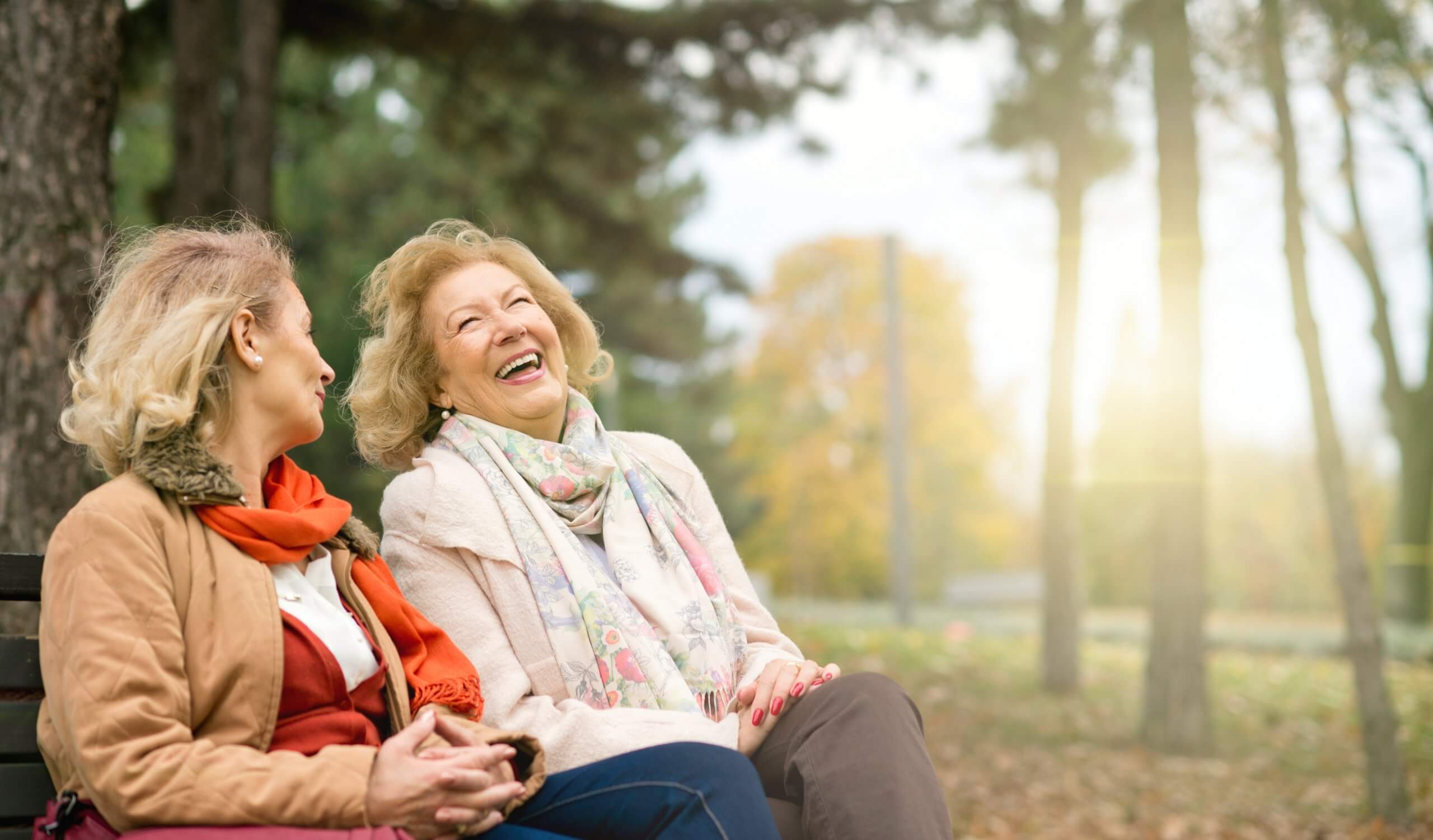 Two laughing senior women sitting on park bench