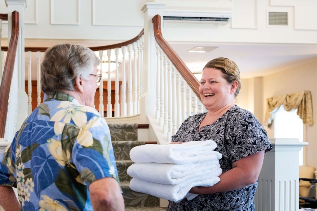 Employee of retirement home handing guest white folded towels