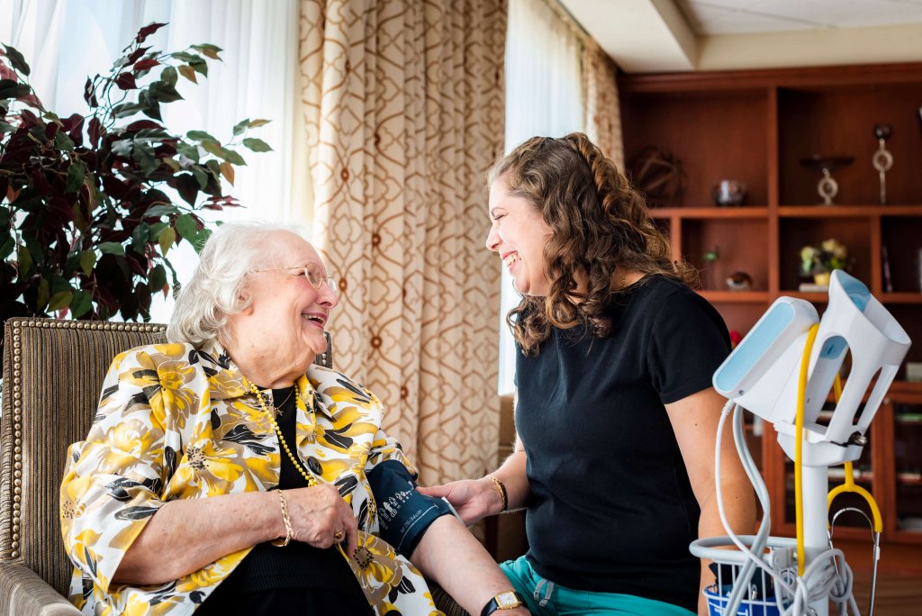 Nurse at retirement home assisting resident while they both laugh