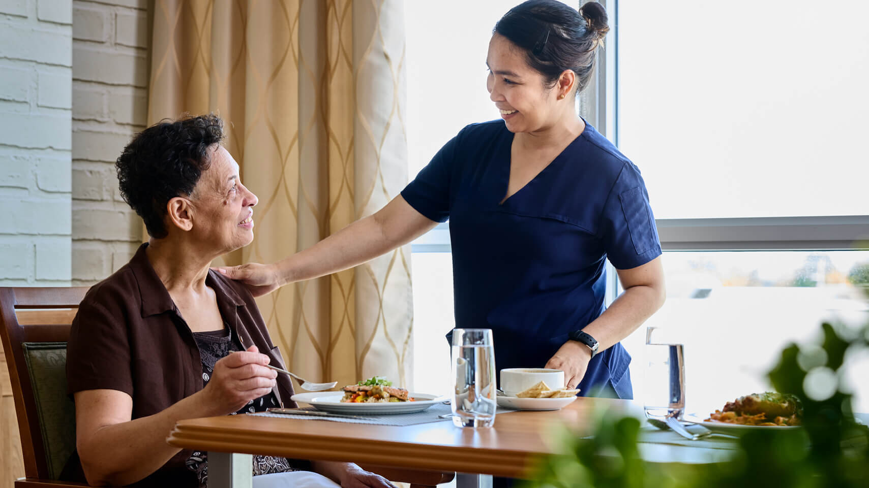 Nurse serving food to a seated resident.