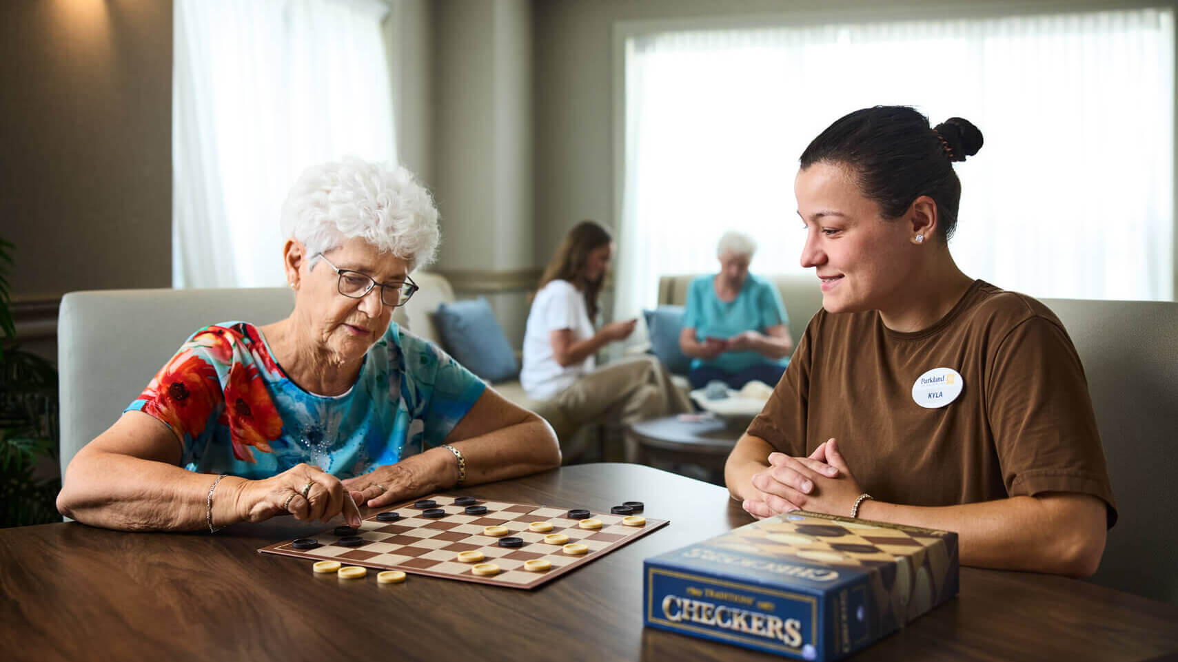 Resident and staff member are seated and playing checkers.